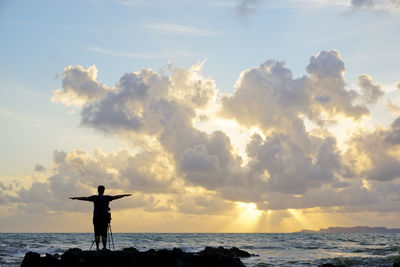 Silhouette of photographer at beach against sky