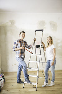 Portrait of young couple standing amidst ladder at home during renovation