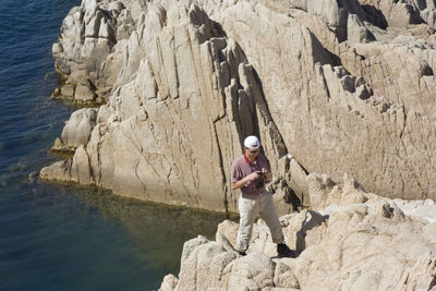 Full length of man with camera standing on cliff by sea during sunny day