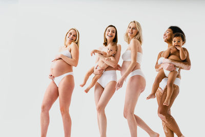 Side view of female friends standing against white background