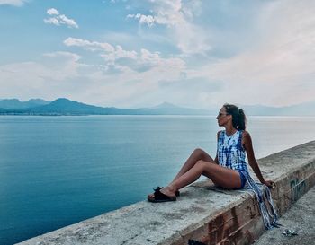 Woman sitting by sea against sky