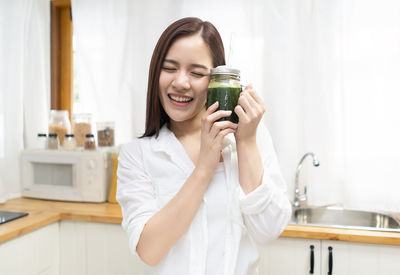 Smiling woman holding smoothie in jar at home