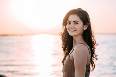 Portrait of smiling young woman standing against sea