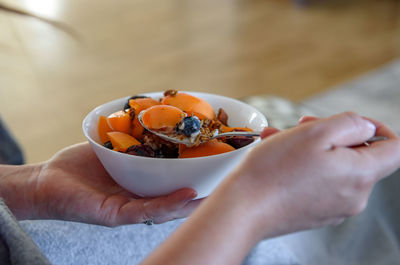 Close-up photo of woman eating overnight oats breakfast with apricots, blueberries and granola
