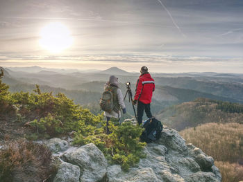 Shooting sunset on top mountain. photographer with eye at viewfinder of camera on tripod at cliff