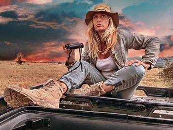 Young woman sitting on road against sky