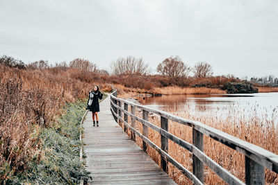 Woman standing on footbridge against clear sky