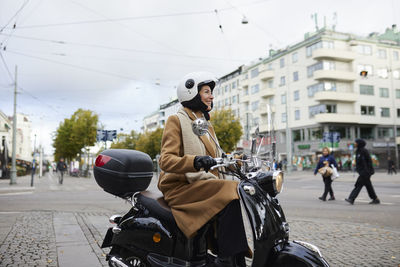 Smiling woman riding scooter in city