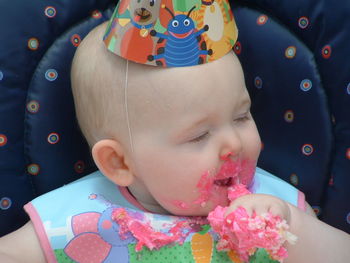 Cute boy wearing party hat eating birthday cake while sitting on chair