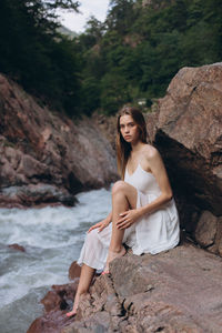 Portrait of young woman sitting on rock by river