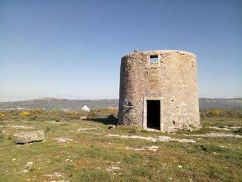 Old built structure on grassy field against clear sky