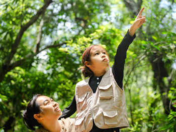 Side view of young woman standing against trees