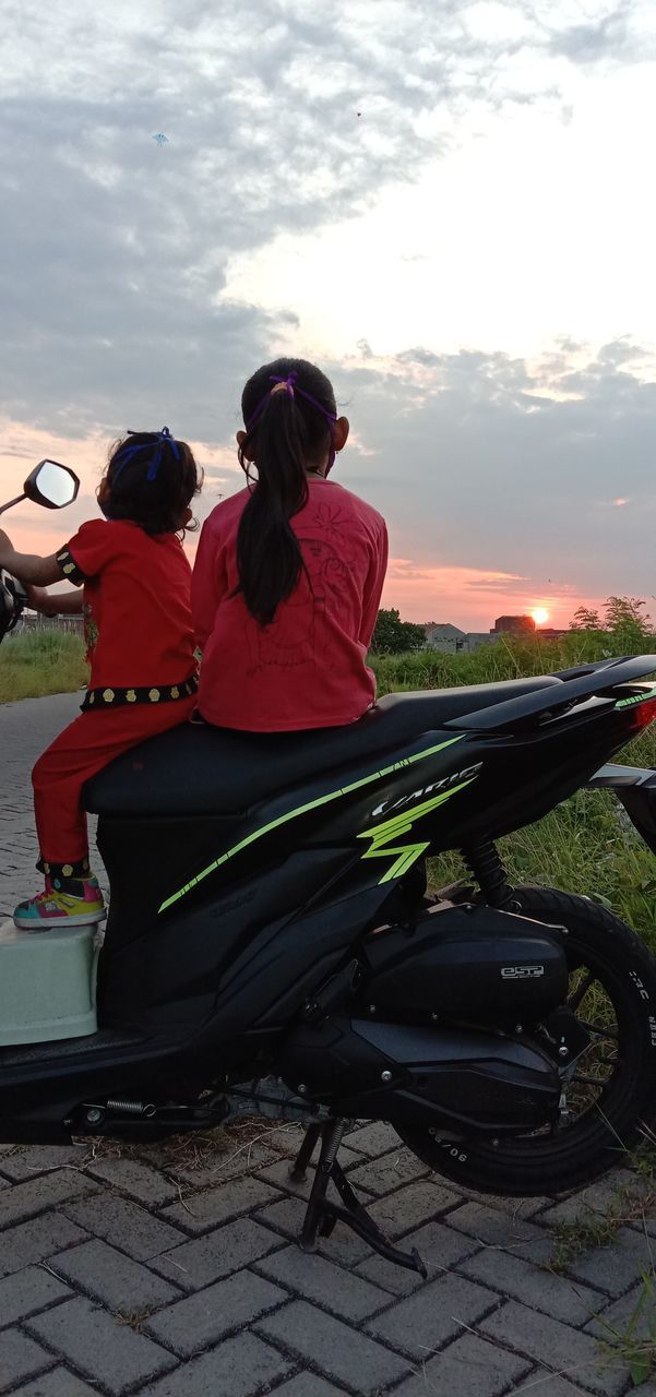 REAR VIEW OF COUPLE SITTING ON ROAD AGAINST SKY