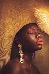 Black woman in large sun hat and statement earrings with eyes closed 