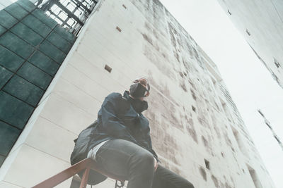 Low angle view of man wearing mask sitting against building