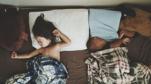 High angle view of siblings sleeping on bed at home