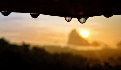 Close-up of water drops on metal against sky during sunset