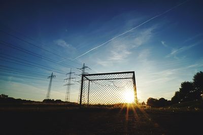 Silhouette electricity pylon on field against sky at sunset