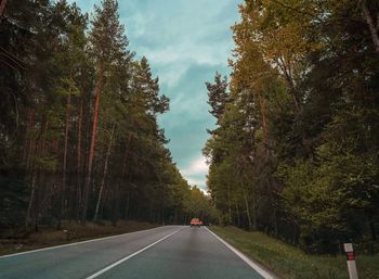 Country road amidst trees against sky