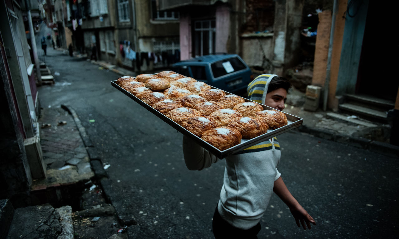 food and drink, one person, food, city, real people, freshness, architecture, street, day, men, incidental people, standing, built structure, focus on foreground, building exterior, container, holding, outdoors, lifestyles, street food