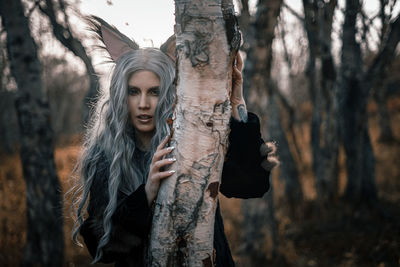 Portrait of woman standing by tree trunk in forest