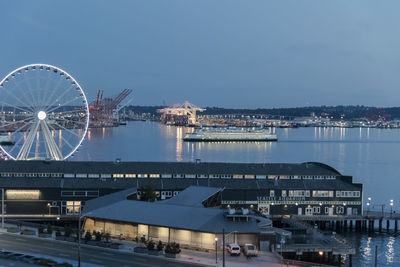 Illuminated ferris wheel in city against sky