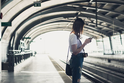 Side view of woman using mobile phone while standing at railroad station platform