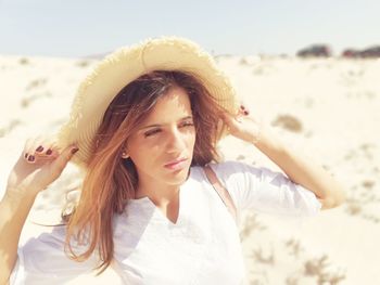 Beautiful young woman holding hat at beach on sunny day