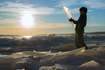Man standing on frozen beach against sky during sunset