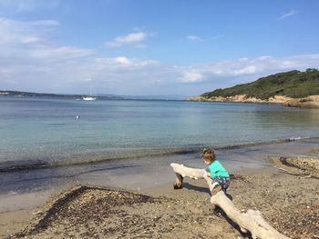 Man sitting on shore at beach against sky