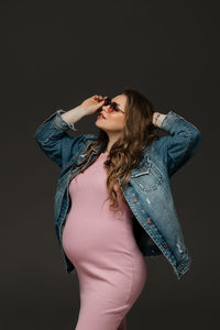 Portrait of young woman standing against black background