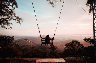 Man sitting on swing at playground against sky