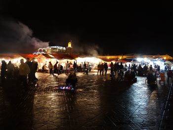 People at illuminated town square against sky at night