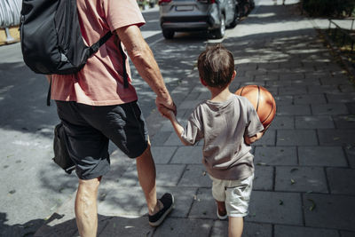 Rear view of man holding hand of grandson while walking on sidewalk