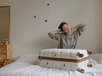 Smiling woman packing her suitcase at home on the white bed