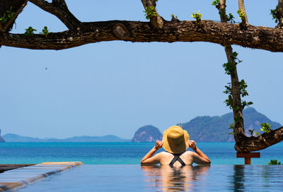 Rear view of woman in swimming pool looking at blue ocean in summer