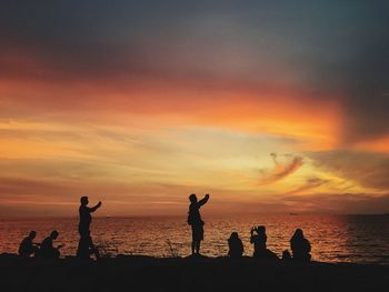 Silhouette people standing at beach during sunset