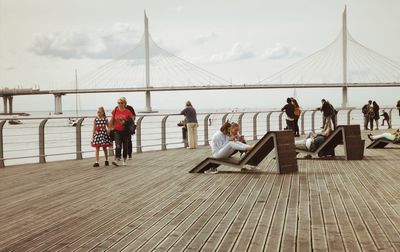 People relaxing on bridge against sky