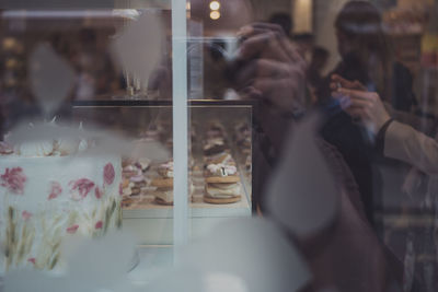 Reflection of people on glass by dessert in display cabinet at bakery shop