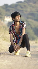 Young man looking away while sitting on land