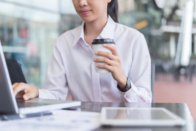 Midsection of woman using mobile phone while sitting on table