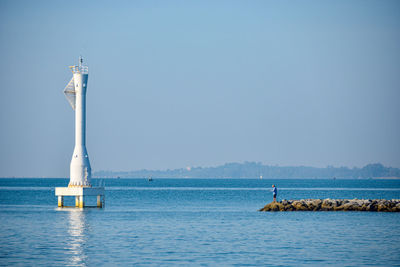 Lighthouse on sea against clear blue sky
