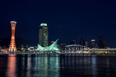 Illuminated city by river against sky at night