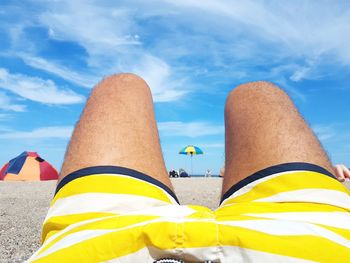 Midsection of man relaxing at beach against sky