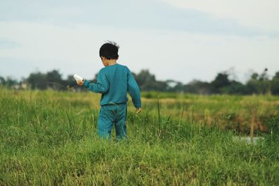 Rear view of boy standing on field against sky