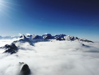 Scenic view of snowcapped mountains amidst clouds against blue sky