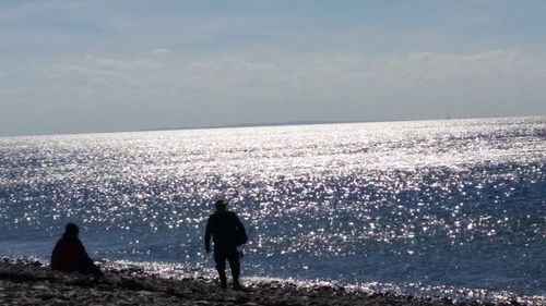 Rear view of silhouette man standing at beach against sky