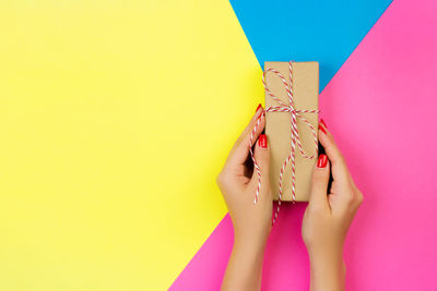 Cropped hands of woman holding gift box on colored background