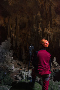 Rear view of man standing by camera in cave