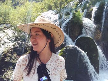 Woman looking away while standing against waterfall in forest